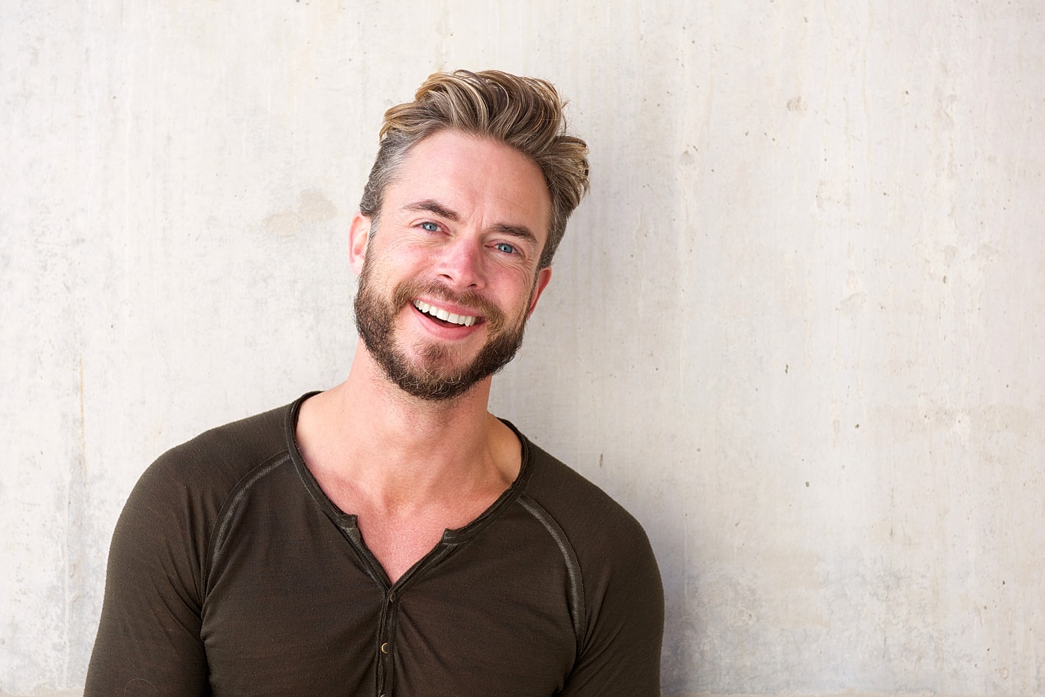 Smiling man with beard against a concrete wall.