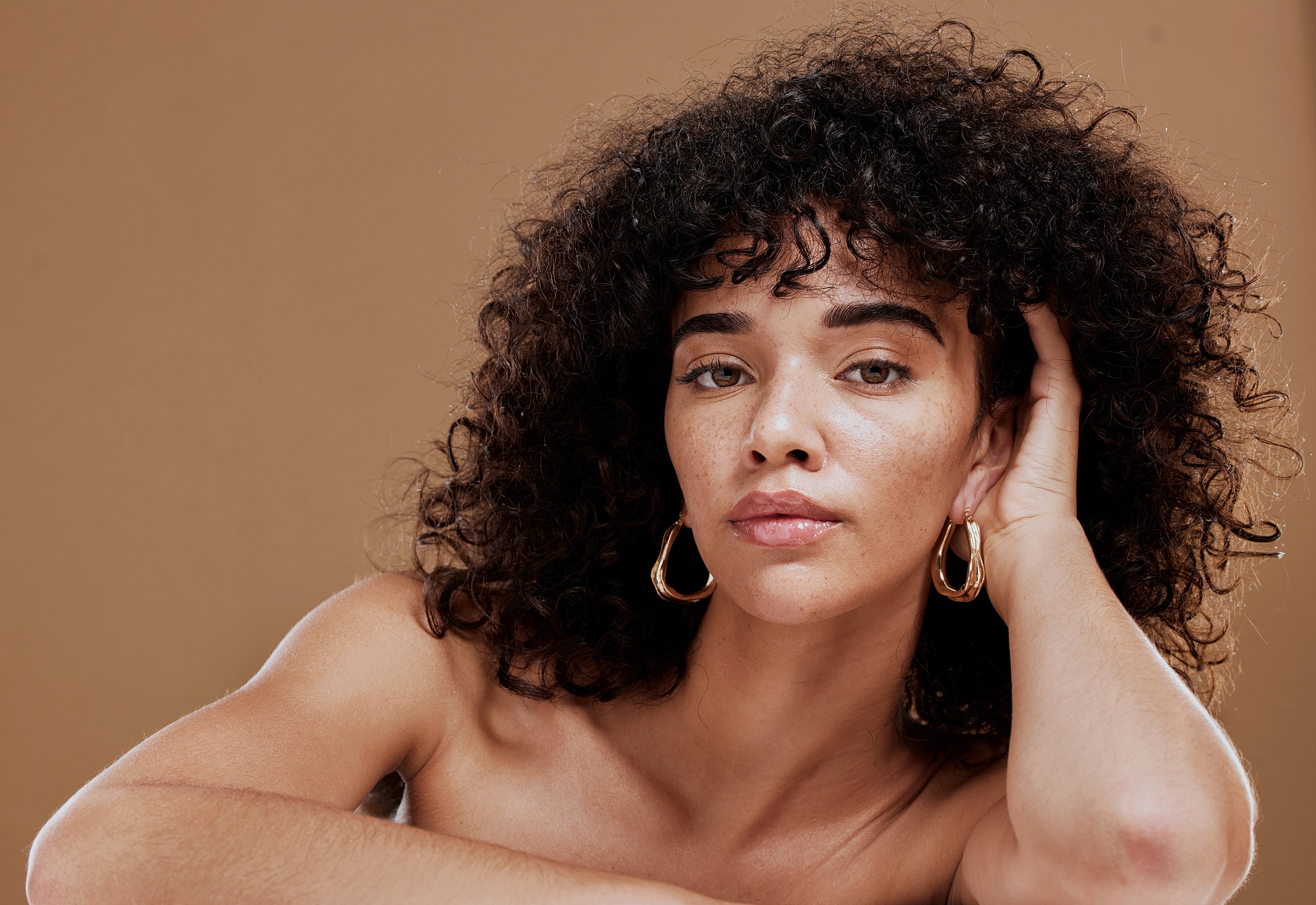 Woman with curly hair and earrings against backdrop.
